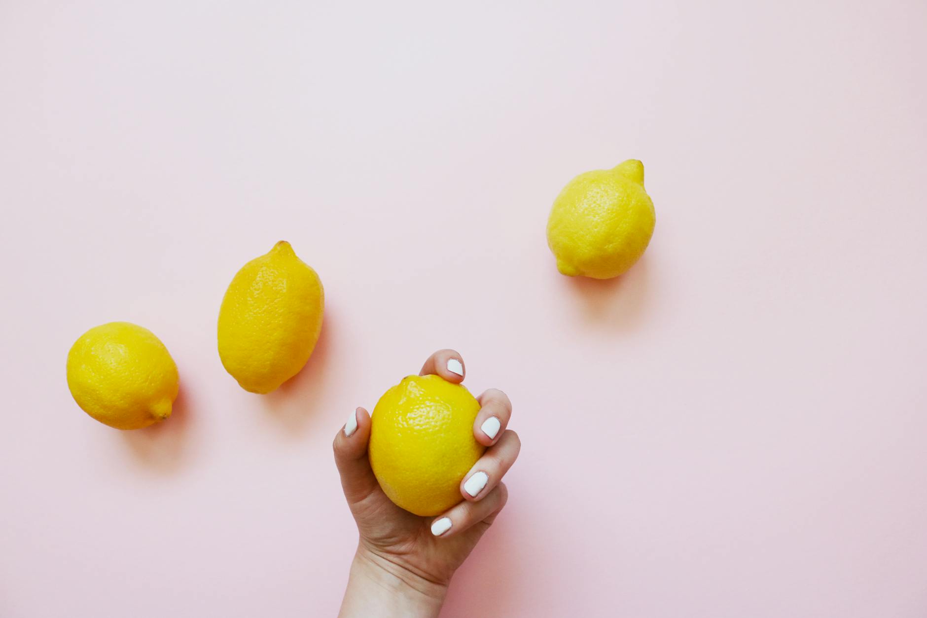 Hand holding a fresh lemon on a soft pink background, symbolizing renewal and change