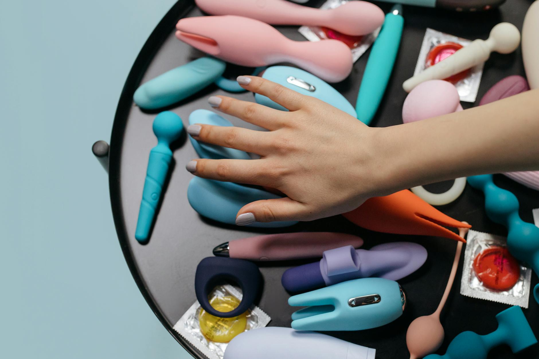 A young woman with eyeglasses holds two colorful vibrators against a purple background.